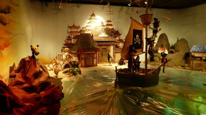 Mehrere Marionetten in einem Bühnenbild mit Meer aus Folie und einem Piratenschiff.