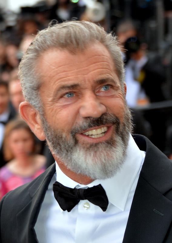Mel Gibson mit grauen Haaren und grauem Bart. Er trägt Anzug und Fliege.