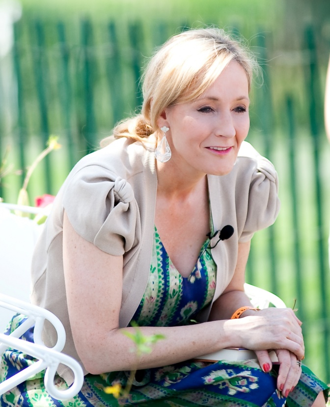 Joanne K. Rowling mit zum Zopf gebundenen langen, glatten Haaren. Sie sitzt auf die Ellbogen gestützt und lächelt.