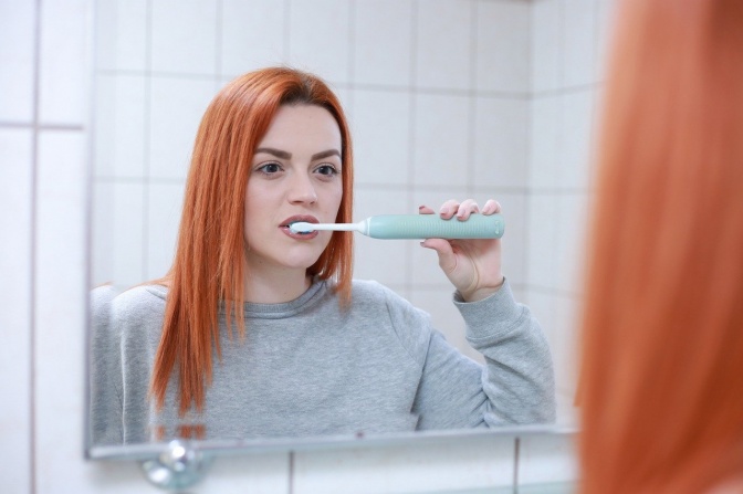 Eine Frau mit langen, glatten Haaren putzt sich vorm Spiegel die Zähne.