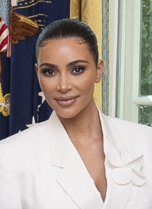 Kim Kardashian in weißem Kostüm. Im Hintergrund sieht man die amerikanische Flagge.