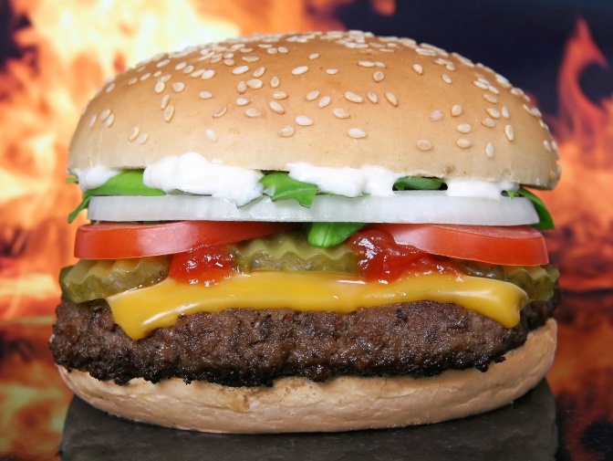 Ein Burger mit Soße und Käse. Im Hintergrund sieht man Flammen.