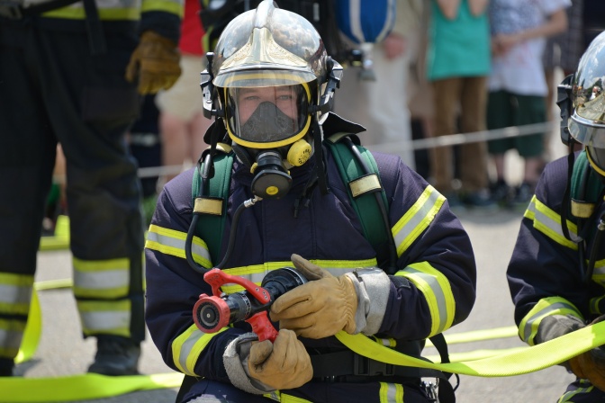 En Feuerwehrmann in Helm und Uniform hält einen Schlauch in der Hand.