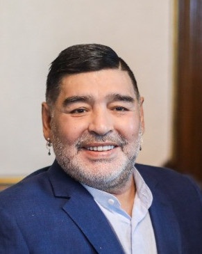 Diego Maradona mit zum Seitenscheitel geegelten Haaren und einem Ohrring. Er trägt Sakko und Hemd.