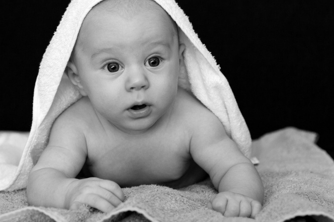 Ein Baby liegt auf einem Handtuch. Das Foto ist in schwarz-weiß.