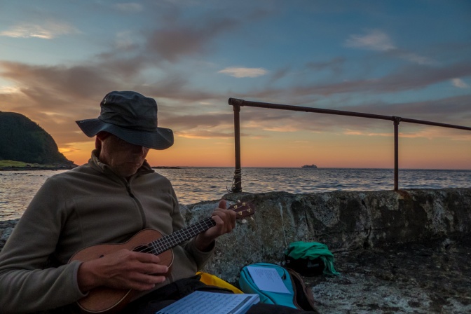 Ein Mann mit Cowboyhut spielt bei Sonnenuntergang Ukulele