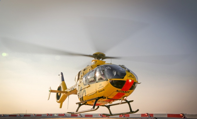 Ein gelber Hubschrauber mit sich drehendem Rotor vor abendlichem Himmel. Auf dem Hubschrauber steht ADAC Luftrettung.