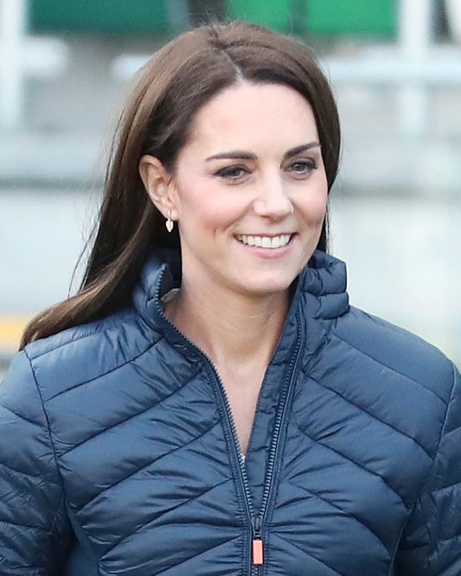 Herzogin Kate mit glatten, langen braunen Haaren in einer dunkelblauen Steppjacke.