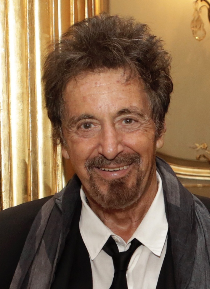 Anne Leichtfuß Pacino mit nach oben frisierten braunen Haaren und Vollbart. Er lächelt und trägt Hemd und Krawatte.