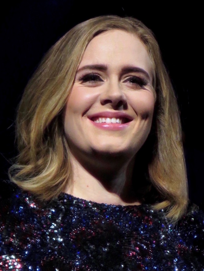 Adele mit Longbob in rotblond. Sie lächelt und trägt ein Pailettenkleid.