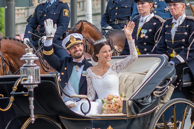 Carl Philip und Sofia in Uniform und Hochzeitskleid in einer Pferdekutsche. Sie winken und lächeln.
