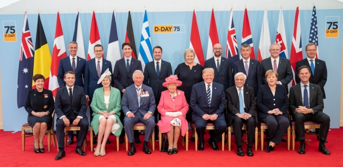 Die Queen und Prinz Charles sitzen in einer Gruppe von Politikern und Politikerinnen vor einer Reihe von Flaggen.