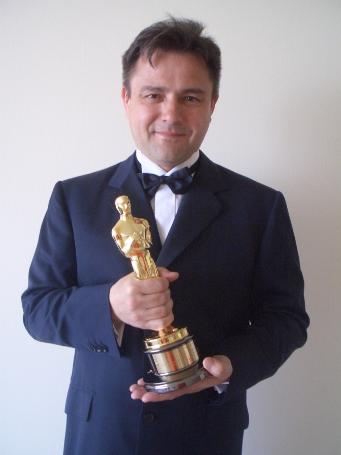 Ein Mann in einem festlichen Anzug hält eine goldene Oscar-Statue in der Hand.