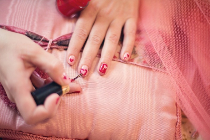 Eine Frau lackiert sich die Fingernägel und malt Herzen darauf.