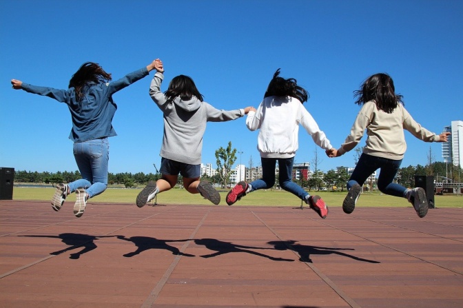 4 Kinder springen in einer Reihe nebeneinander in die Luft. Sie wurden von hinten fotografiert.