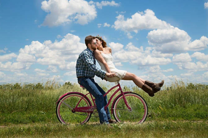 Ein Mann fährt Fahrrad, eine Frau sitzt auf dem Lenker. Die beiden küssen sich.