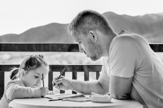 Ein Mann und ein kleines Mädchen sitzen an einem Tisch am Meer und zeichnen