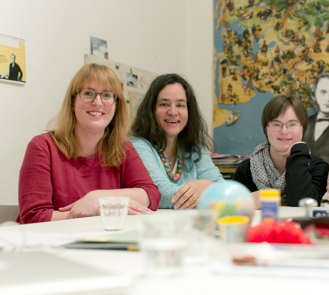 Drei Frauen, eine davon mit Down-Syndrom, sitzen nebeneinander an einem Tisch.