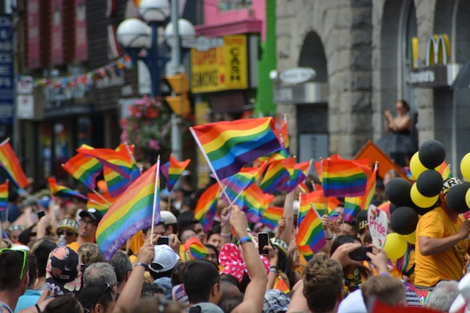 Eine große Gruppe an Menschen winkt mit Regenbogenflaggen