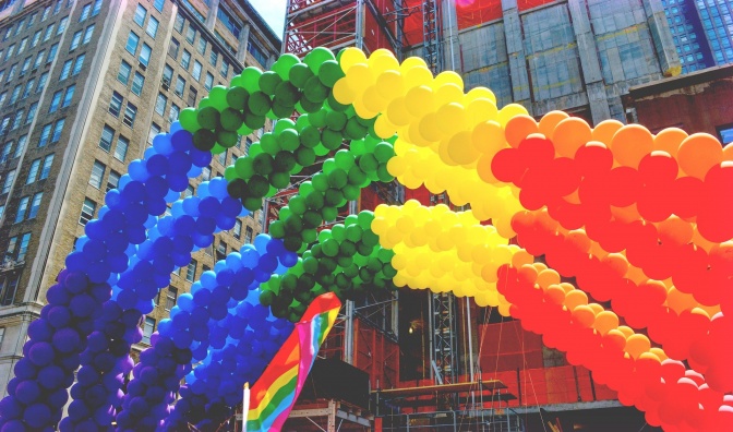 Lange Schlangen regenbogenfarbener Luftballons, darunter eine Regenbogenflagge