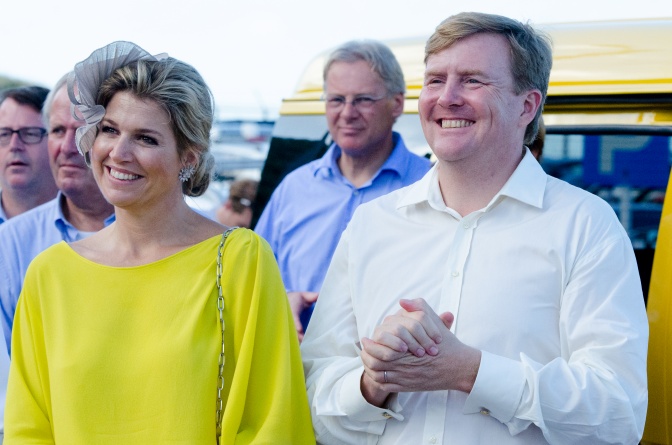 Willem-Alexander und Máxima der Niederlande stehen lächelnd nebeneinander, im Hintergrund andere Menschen