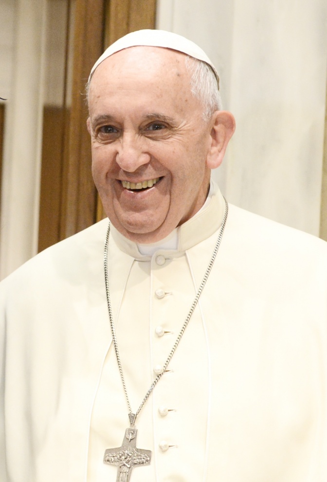 Papst Franziskus in weißer Kleidung mit einem großen Kreuz um den Hals. Er lächelt.