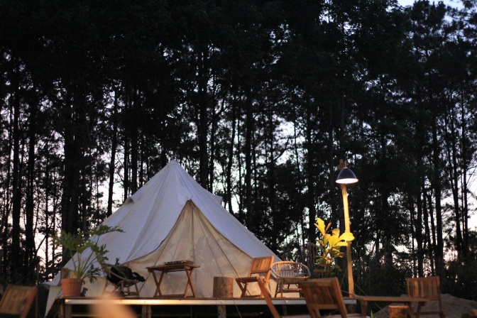 Ein weißes Zelt auf einem Holzpodest, davor ein Grill und einige Sitzmöbel.