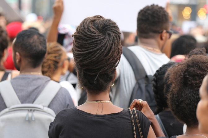 Mehrere Menschen demonstrieren, unter anderem eine schwarze Frau mit aufwendig geflochtenen Haaren