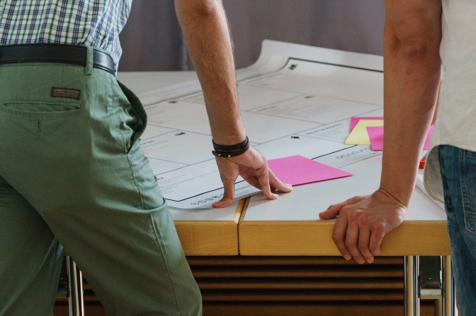 2 Männer beugen sich über einen Tisch mit Plänen und Unterlagen