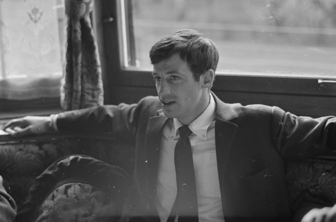 Ein schwarz-weiß-Foto von Jean-Paul Belmondo als hutaussehendem jungen Mann in Anzug und Krawatte
