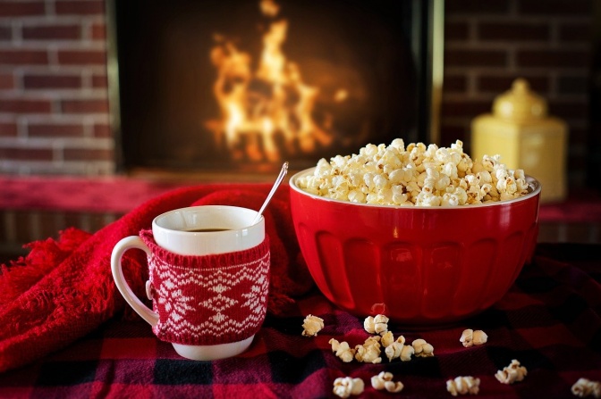 Eine Schüssel Popcorn und eine Tasse mit einem Getränk stehen auf einem Tisch vor einem brennenden Kamin