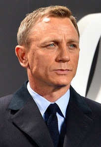 Daniel Craig steht in Anzug und Krawatte vor einem 007-Schriftzug