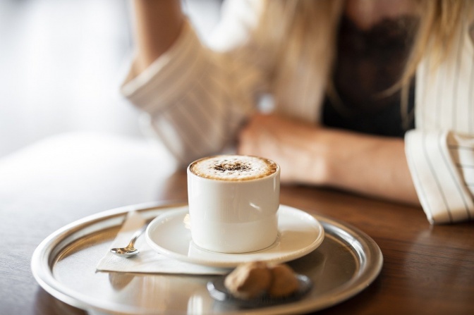 Eine Frau sitzt vor einem Silbertablett mit einer Tasse Kaffee und einem Keks