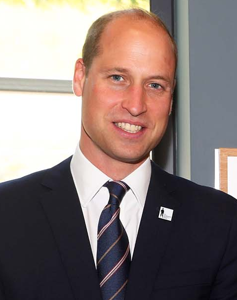 Prinz William mit Stirnglatze in Anzug und Krawatte. Er lächelt.