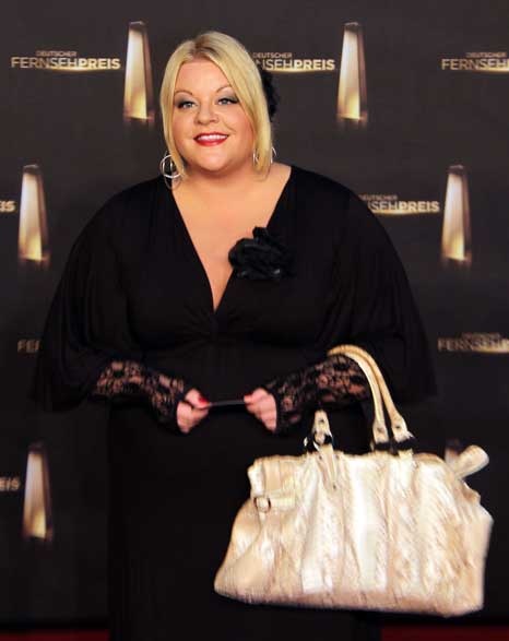 Tine Wittler in schwarzer Kleidung mit großer Handtasche vor einer Logowand des deutschen Fernsehpreises