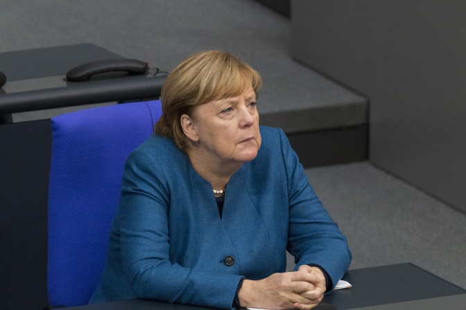 Angela Merkel sitzt mit ernstem Blick auf einem Stuhl im Bundestag.