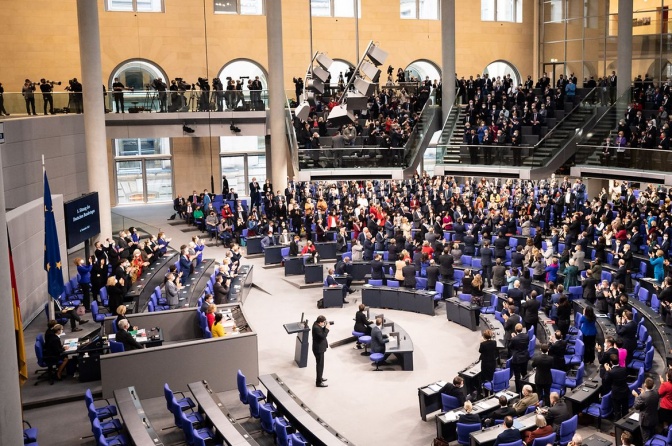 Politiker:innen auf den kreisförmig angeordneten Sitzen im Bundestag. Alle schauen zu Olaf Scholz und klatschen.