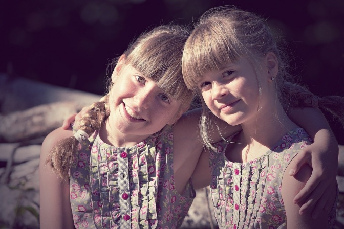 2 blonde Mädchen im Grundschulalter mit geflochtenen Zöpfen in einheitlichen Blümchenkleidern