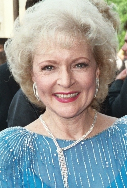 Betty White in einem hellblauen Pailettenkleid mit Make up und Schmuck. Sie lächelt in die Kamera.