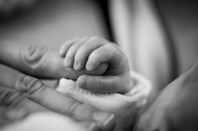 Schwarz-weiß Foto einer Baby-Hand, die den Finger einer Erwachsenen umfasst