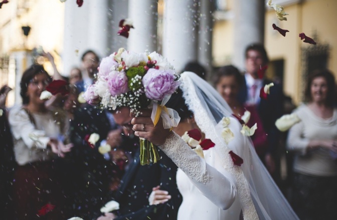 Ein Hochzeitspaar wird mit Reis beworfen und versteckt sich hinter dem Brautstrauß