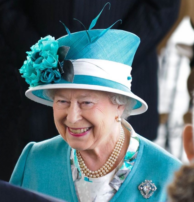 Die Queen lächelnd mit einem auffälligen Hut mit Blumenschmuck