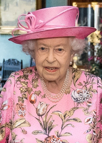 Die Queen mit weißen Locken in einem geblümten Kleid mit passendem Schmuck und Hut.