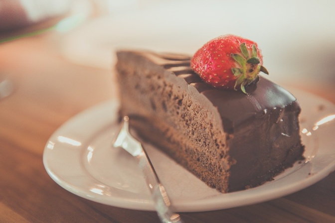Ein Stück Schokoladenkuchen auf einem Teller, obendrauf eine Erdbeere