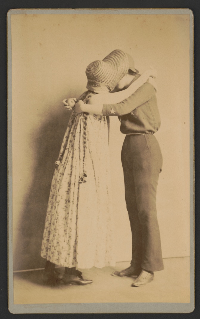 Schwarz-weiß-Foto zweier sich umarmender, sich küssender Frauen, eine in femininer, eine in maskuliner Kleidung