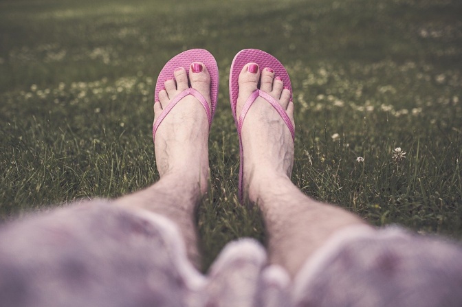 Behaarte Beine mit lackierten Fußnägeln und pinken Flipflops