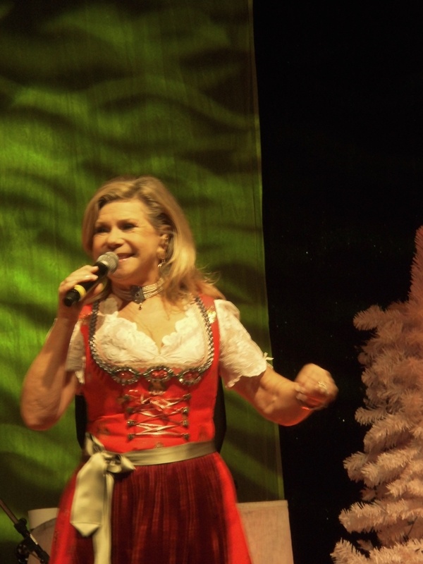 Marianne Hartl steht im Dirndl auf der Bühne und singt in ein Mikro.