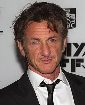 Sean Penn in Anzug und Krawatte. Eine Locke fällt ihm ins Gesicht. Er steht vor einer Logowand.