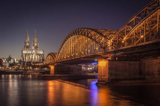 Eine Rheinbrücke und der Kölner Dom in farbiger Beleuchtung