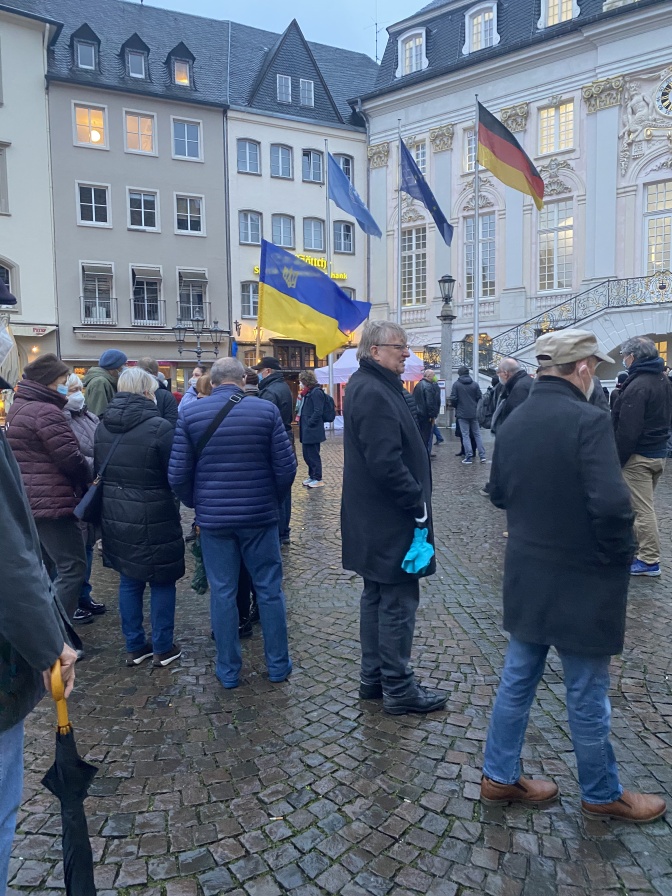 Menschen stehen zusammen vor dem Bonner Rathaus, ein Mann hält eine große ukrainische Flagge.